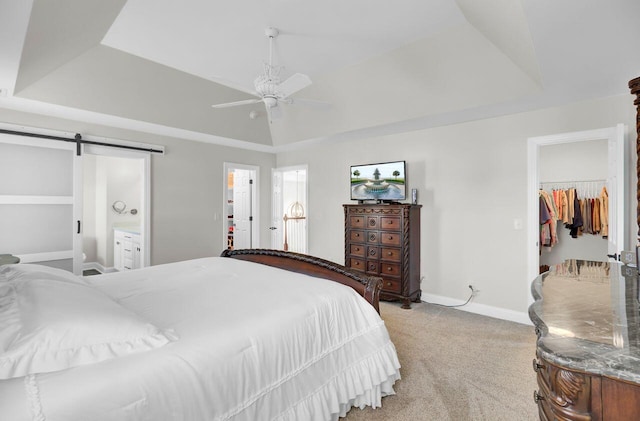 carpeted bedroom with a tray ceiling, a walk in closet, a barn door, and ceiling fan