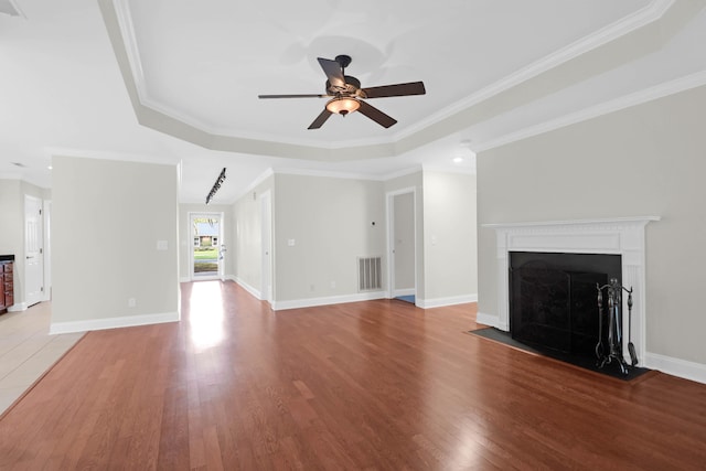 unfurnished living room featuring a raised ceiling, wood-type flooring, and crown molding