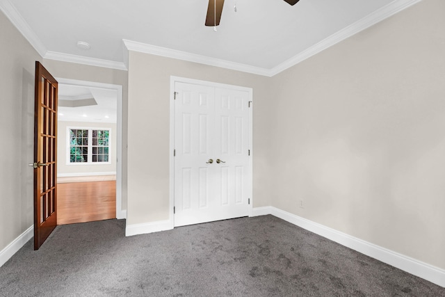 unfurnished bedroom with ceiling fan, a closet, crown molding, and dark carpet