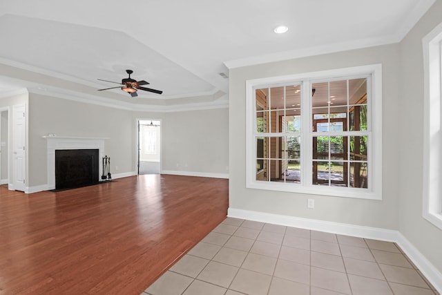 unfurnished living room featuring a raised ceiling, ceiling fan, ornamental molding, and light tile patterned flooring