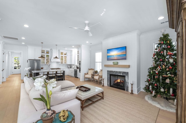 living room featuring recessed lighting, visible vents, a premium fireplace, and light wood finished floors