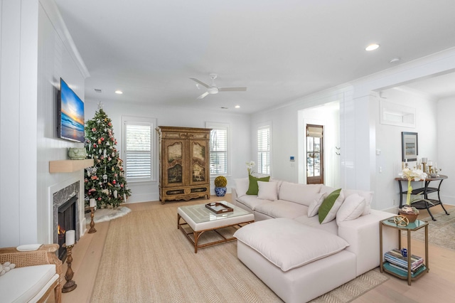 living room featuring ornamental molding, recessed lighting, a warm lit fireplace, wood finished floors, and a ceiling fan