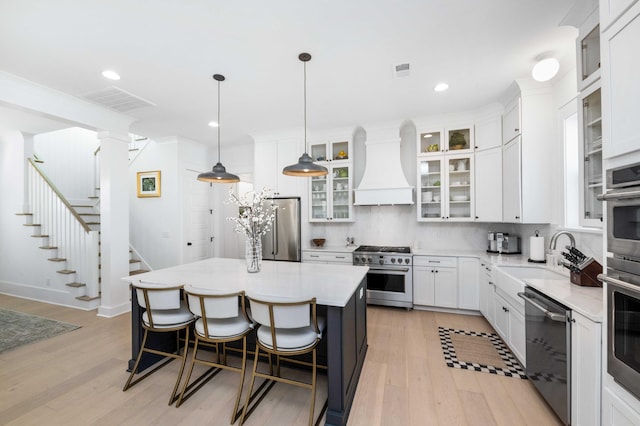 kitchen with premium range hood, visible vents, high quality appliances, a breakfast bar, and a sink