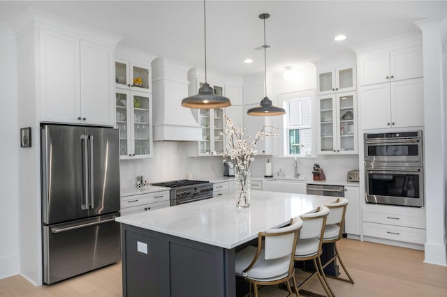 kitchen featuring backsplash, premium range hood, high quality appliances, white cabinetry, and a sink