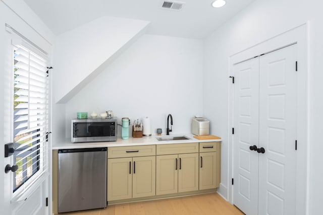 kitchen featuring stainless steel microwave, visible vents, light wood-type flooring, refrigerator, and a sink