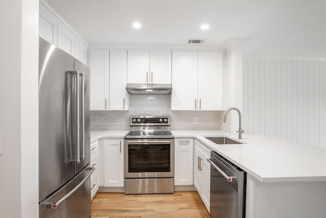 kitchen with light countertops, appliances with stainless steel finishes, white cabinets, a sink, and under cabinet range hood