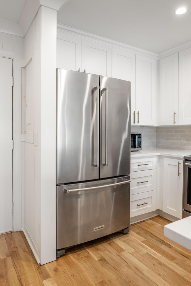 kitchen featuring stainless steel appliances, tasteful backsplash, light countertops, light wood-style flooring, and white cabinetry