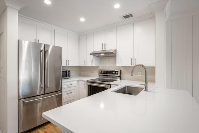 kitchen with under cabinet range hood, a sink, visible vents, light countertops, and appliances with stainless steel finishes