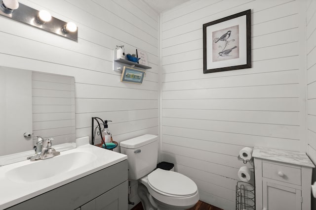 bathroom featuring vanity, wooden walls, and toilet