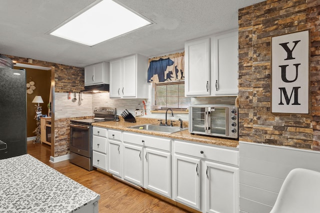 kitchen with electric range oven, white cabinets, sink, and light wood-type flooring