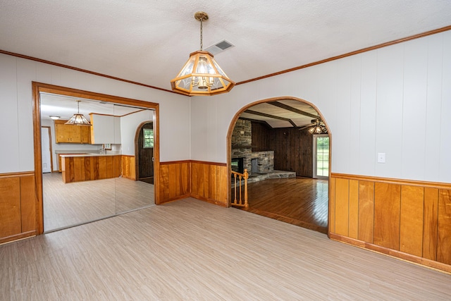 unfurnished dining area featuring wood finished floors, ceiling fan, arched walkways, wooden walls, and ornamental molding