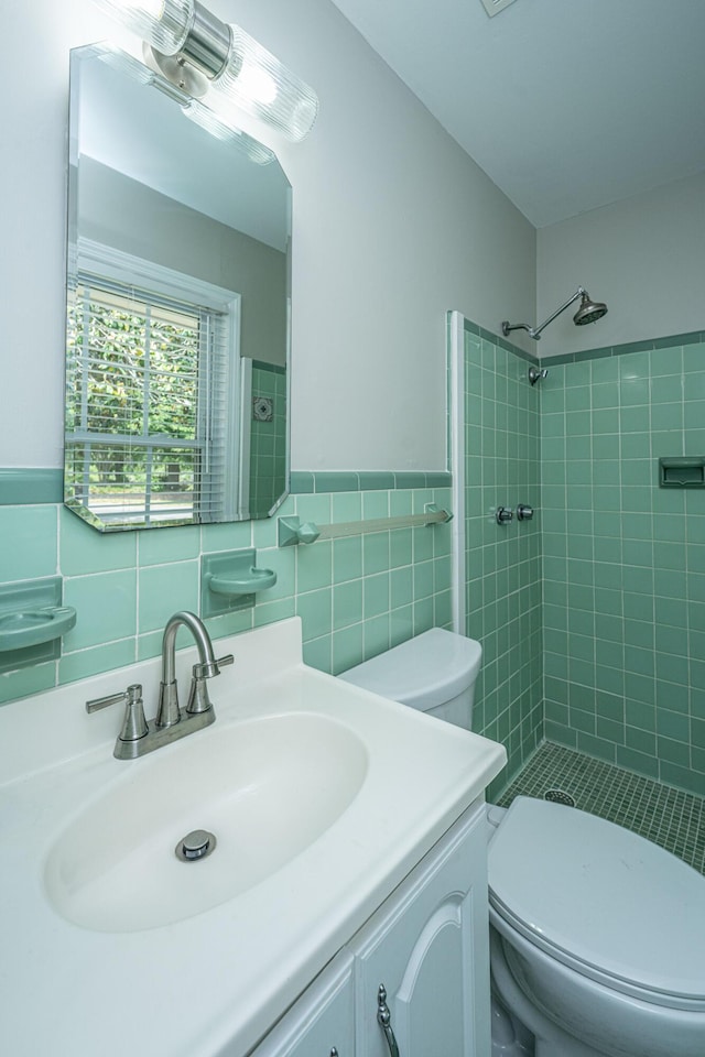 bathroom with toilet, tile walls, tiled shower, and vanity