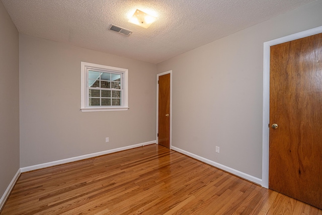empty room with light wood-style flooring, a textured ceiling, baseboards, and visible vents