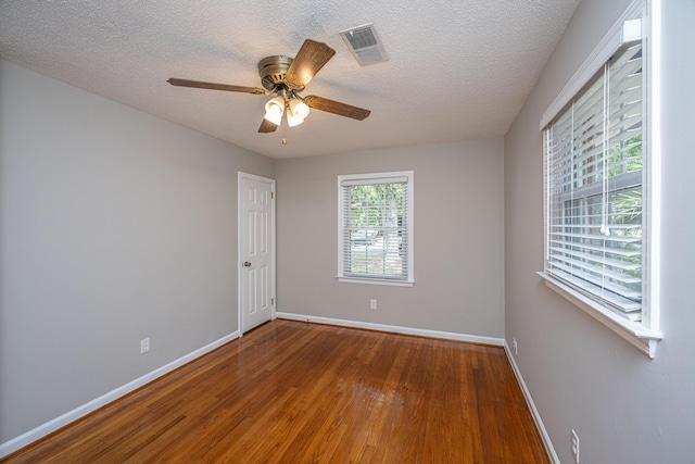 empty room featuring a textured ceiling, baseboards, ceiling fan, visible vents, and wood-type flooring