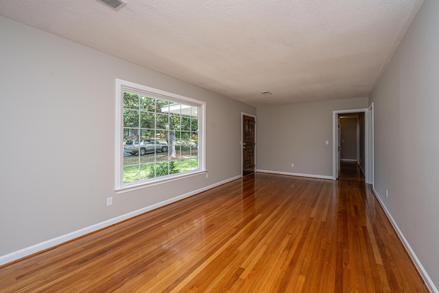 spare room featuring baseboards, hardwood / wood-style floors, and a textured ceiling
