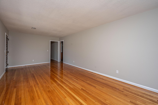 empty room with a textured ceiling, light wood-style flooring, and baseboards