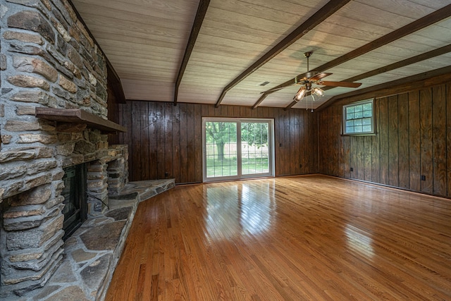 unfurnished living room with hardwood / wood-style floors, ceiling fan, wooden walls, a stone fireplace, and vaulted ceiling with beams