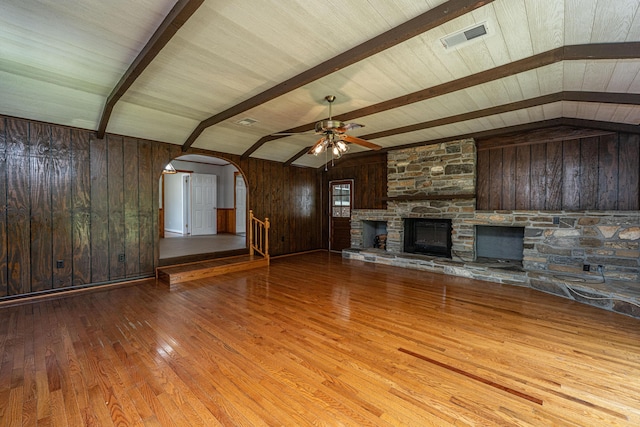 unfurnished living room featuring lofted ceiling with beams, visible vents, ceiling fan, wooden walls, and wood-type flooring