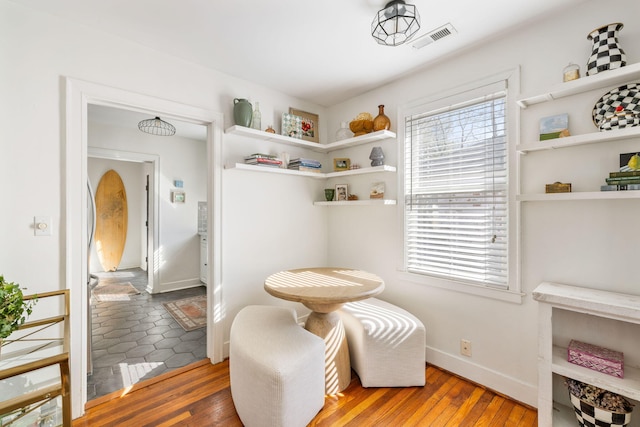 living area with wood-type flooring, visible vents, and baseboards