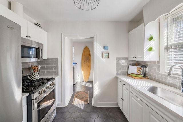 kitchen with a sink, white cabinets, light countertops, appliances with stainless steel finishes, and backsplash