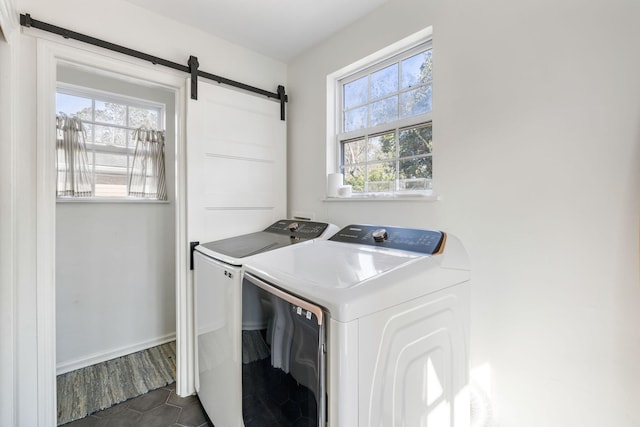 laundry room featuring laundry area, a barn door, washing machine and dryer, and baseboards