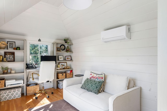 living area with vaulted ceiling, an AC wall unit, and wood finished floors