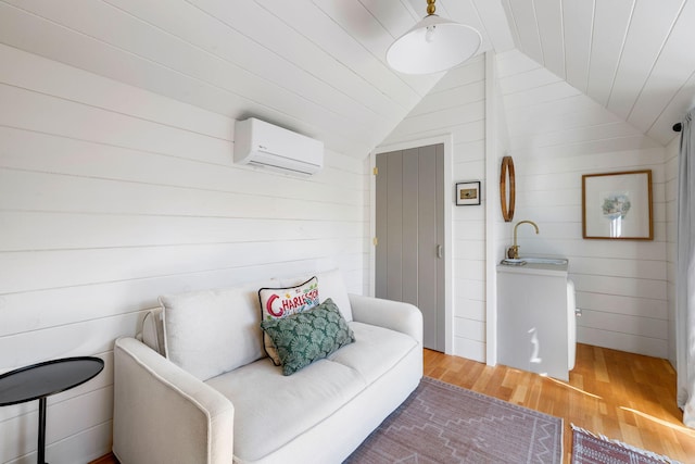 living room featuring wooden walls, an AC wall unit, vaulted ceiling, and light wood-style flooring