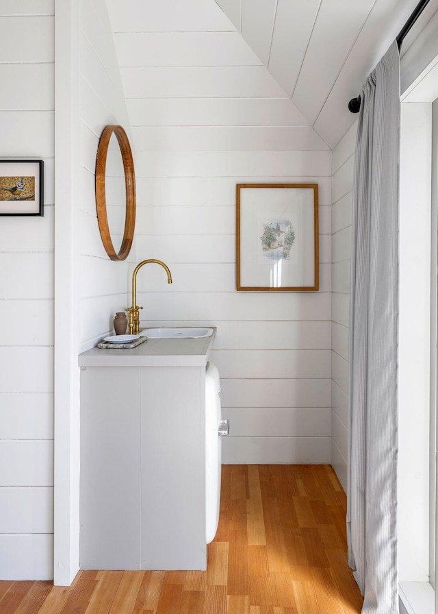 bathroom with vaulted ceiling, a sink, and wood finished floors