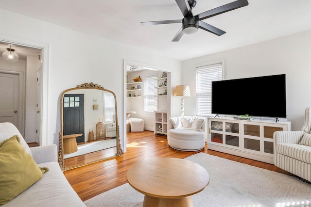 living area featuring arched walkways, wood finished floors, a ceiling fan, and built in features