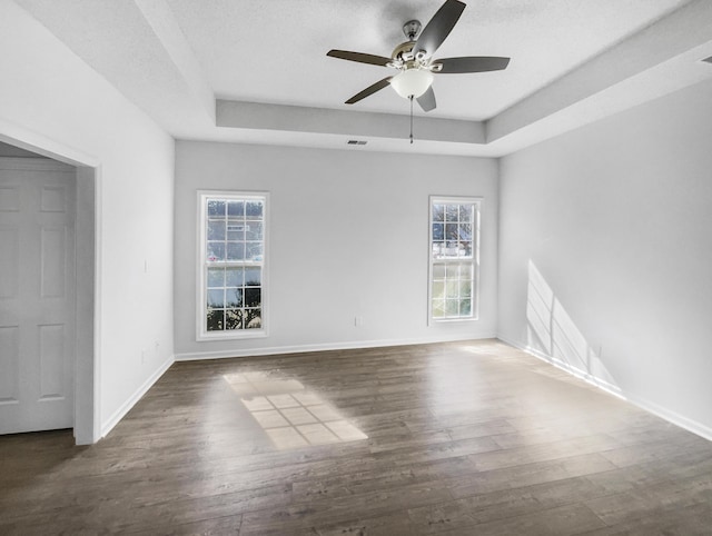 unfurnished room featuring a ceiling fan, a raised ceiling, dark wood finished floors, and baseboards