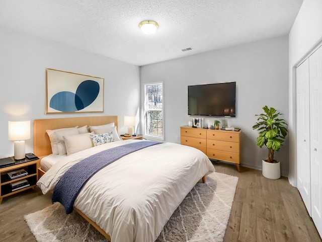 bedroom with a textured ceiling, a closet, wood finished floors, and visible vents