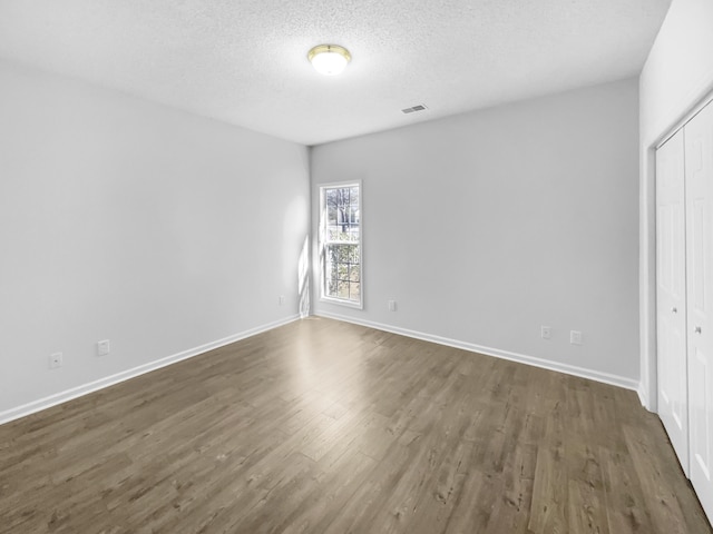 unfurnished bedroom with dark wood-style flooring, a closet, visible vents, a textured ceiling, and baseboards