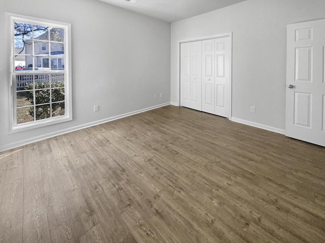 unfurnished bedroom with a closet, dark wood-style flooring, and baseboards