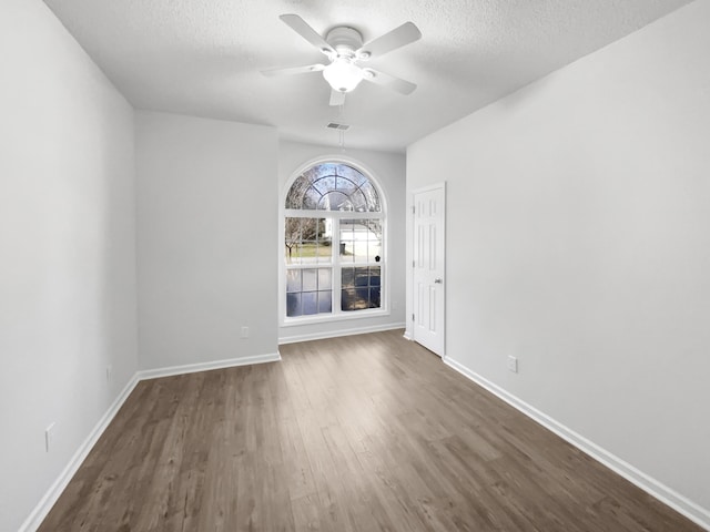 unfurnished room featuring dark wood-type flooring, ceiling fan, a textured ceiling, and baseboards