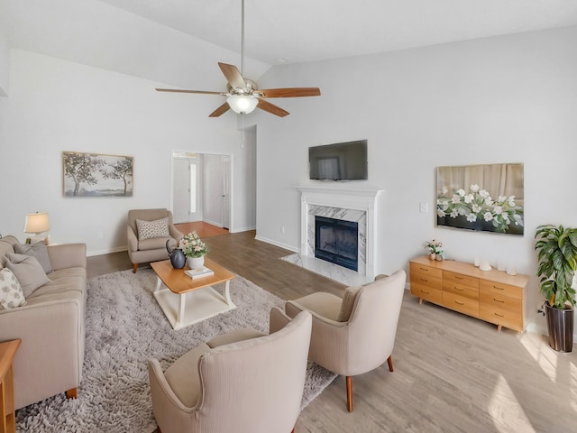 living room featuring ceiling fan, a premium fireplace, wood finished floors, and baseboards