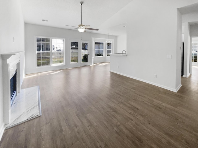 unfurnished living room featuring a premium fireplace, a ceiling fan, visible vents, baseboards, and dark wood finished floors