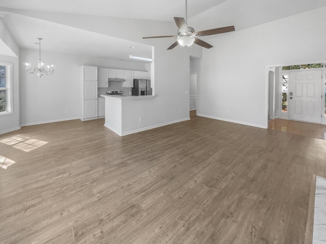 unfurnished living room featuring lofted ceiling, ceiling fan with notable chandelier, wood finished floors, and baseboards