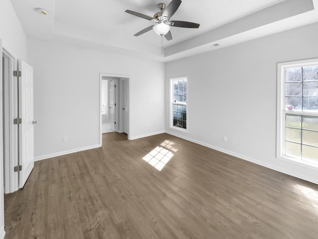 unfurnished bedroom featuring baseboards, multiple windows, a tray ceiling, and dark wood-style flooring