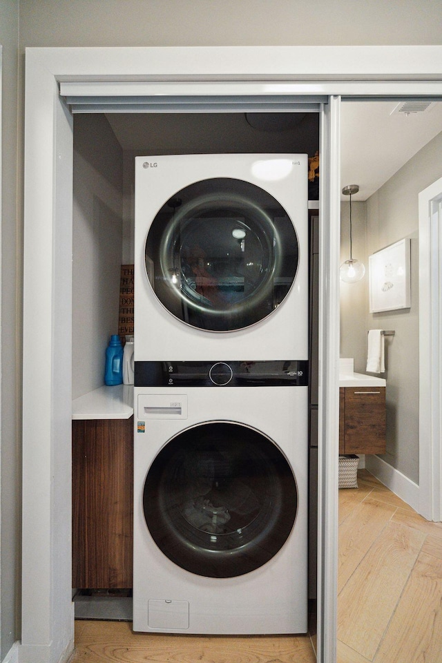 clothes washing area featuring stacked washer and clothes dryer, light wood-style flooring, and baseboards