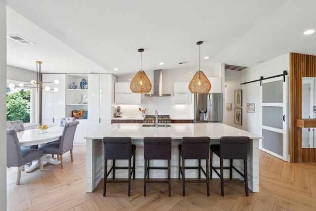 kitchen featuring wall chimney range hood, stainless steel fridge, white cabinets, light countertops, and recessed lighting