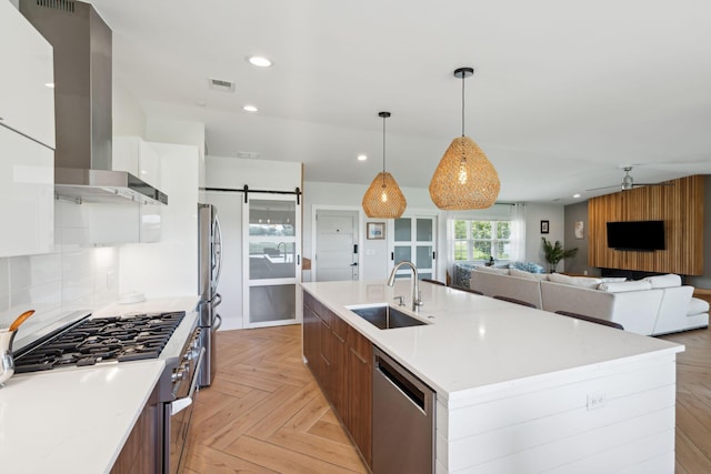kitchen featuring a sink, stainless steel appliances, wall chimney range hood, modern cabinets, and a center island with sink