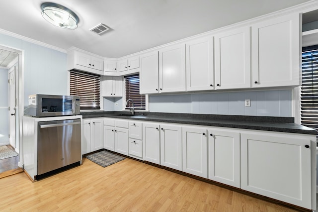 kitchen with appliances with stainless steel finishes, crown molding, light wood-style floors, white cabinetry, and a sink