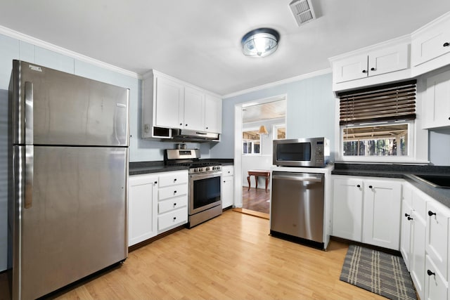 kitchen with stainless steel appliances, dark countertops, ornamental molding, light wood-style floors, and white cabinetry