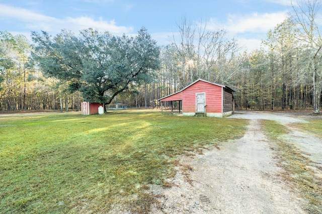 view of yard featuring an outbuilding, dirt driveway, a storage shed, and a view of trees