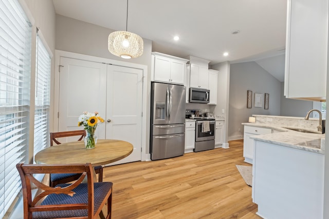 kitchen with stainless steel appliances, a sink, white cabinets, light wood-style floors, and light stone counters