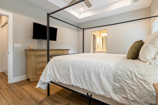 bedroom with a raised ceiling, light wood finished floors, baseboards, a ceiling fan, and ensuite bathroom