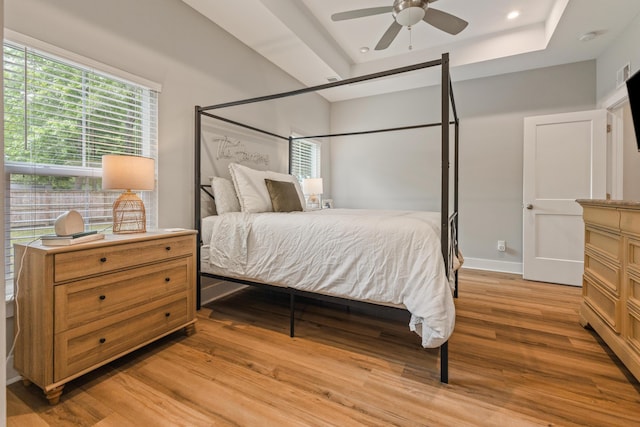 bedroom featuring light wood finished floors, a raised ceiling, multiple windows, recessed lighting, and a ceiling fan