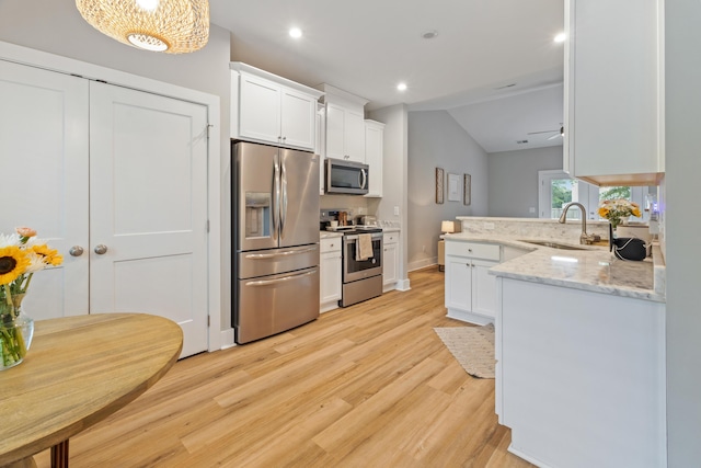 kitchen featuring appliances with stainless steel finishes, a sink, white cabinets, a peninsula, and light wood-style floors