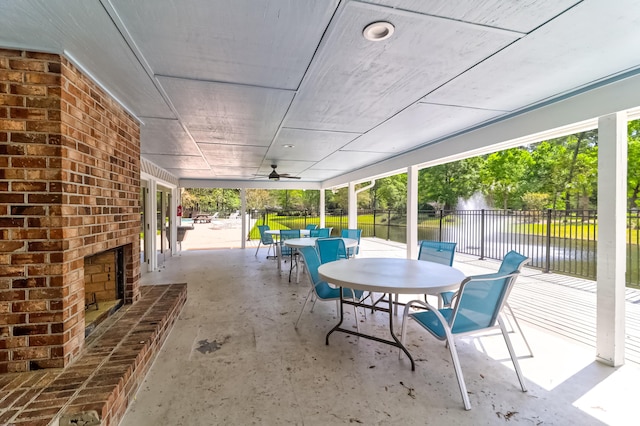 view of patio with an outdoor brick fireplace, a water view, and ceiling fan