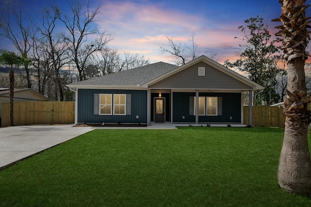 back of property at dusk with a porch, fence, roof with shingles, a lawn, and board and batten siding